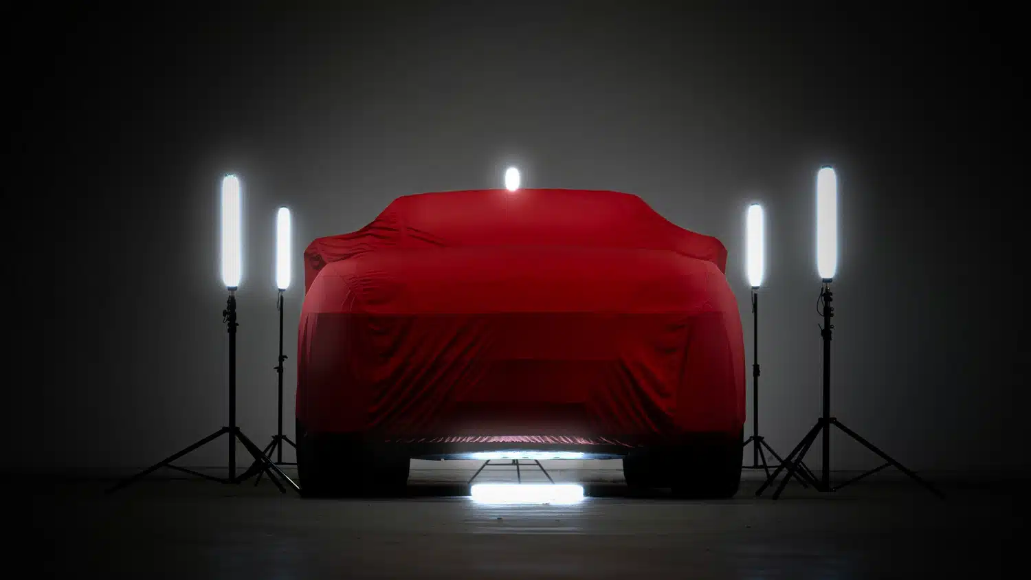 2021 Lamborghini Urus V8 Auto shrouded with a red car cover, surrounded by bright, cool, white, light bars