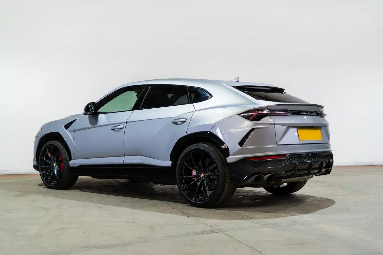 A grey, 2021 Lamborghini Urus V8 Auto, rear end facing the viewer, in front of a white wall, in a warehouse