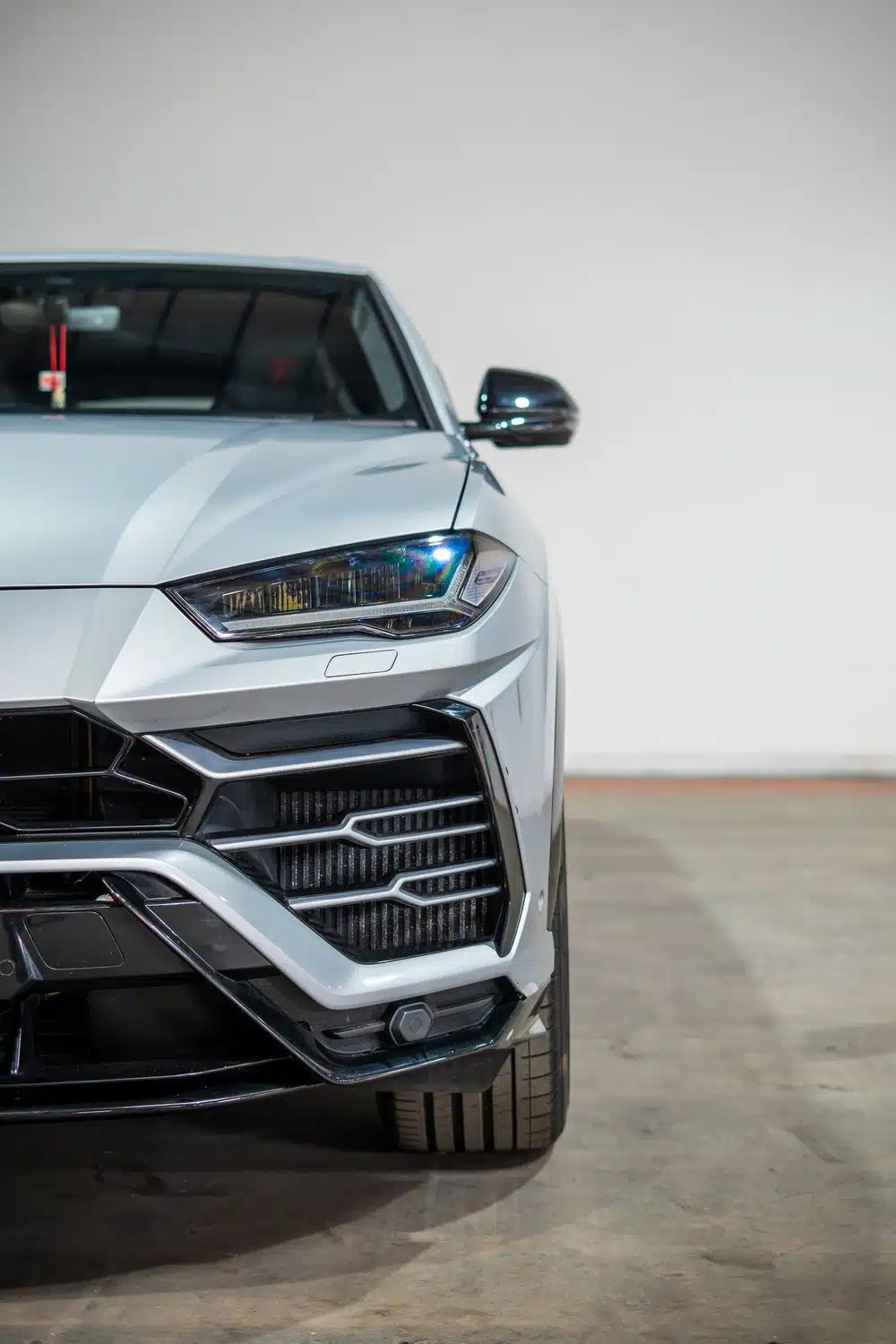 A grey, 2021 Lamborghini Urus V8 Auto, facing forwards, in front of a white wall, in a warehouse