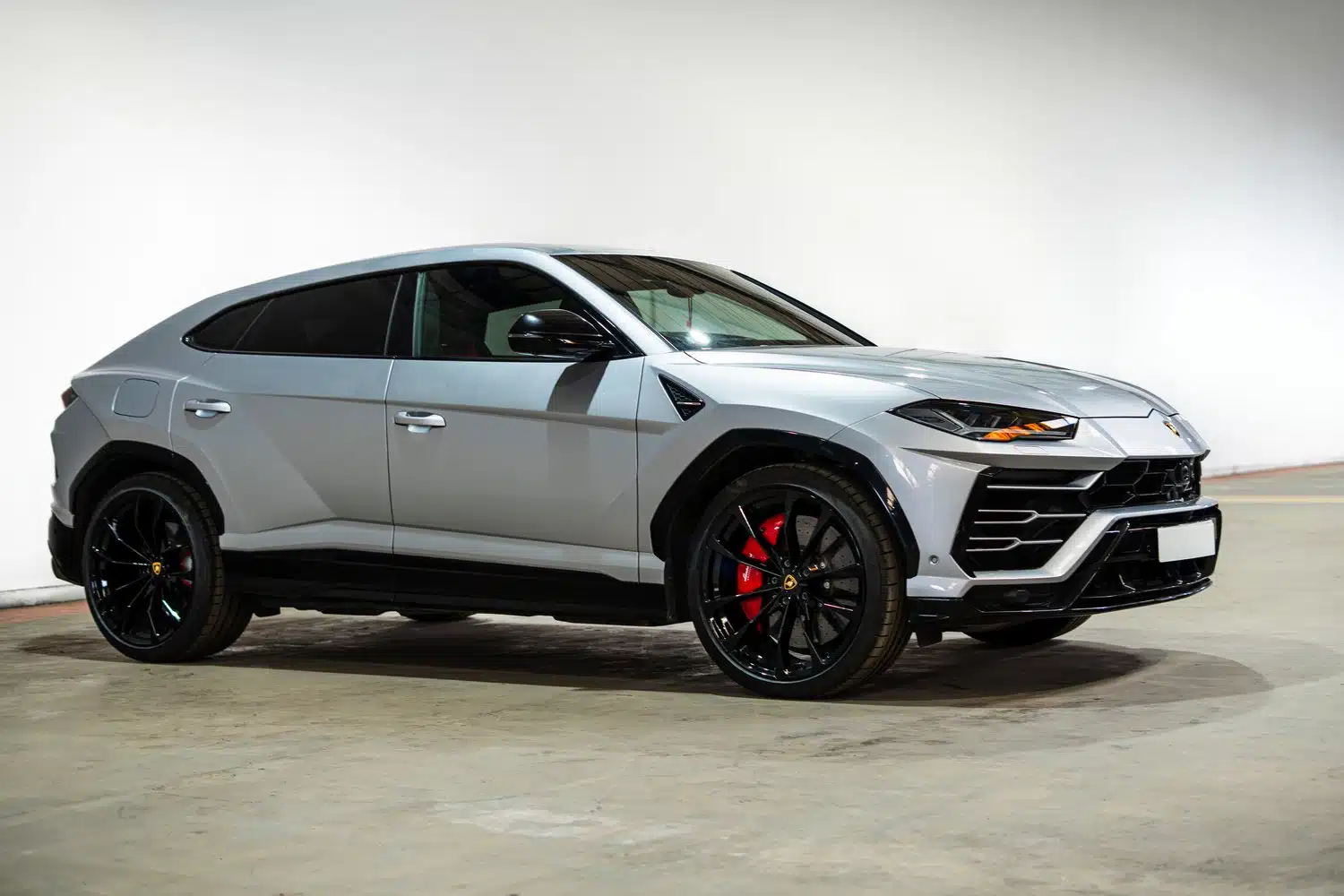 A grey, 2021 Lamborghini Urus V8 Auto, sideways on, in front of an white wall, in a warehouse