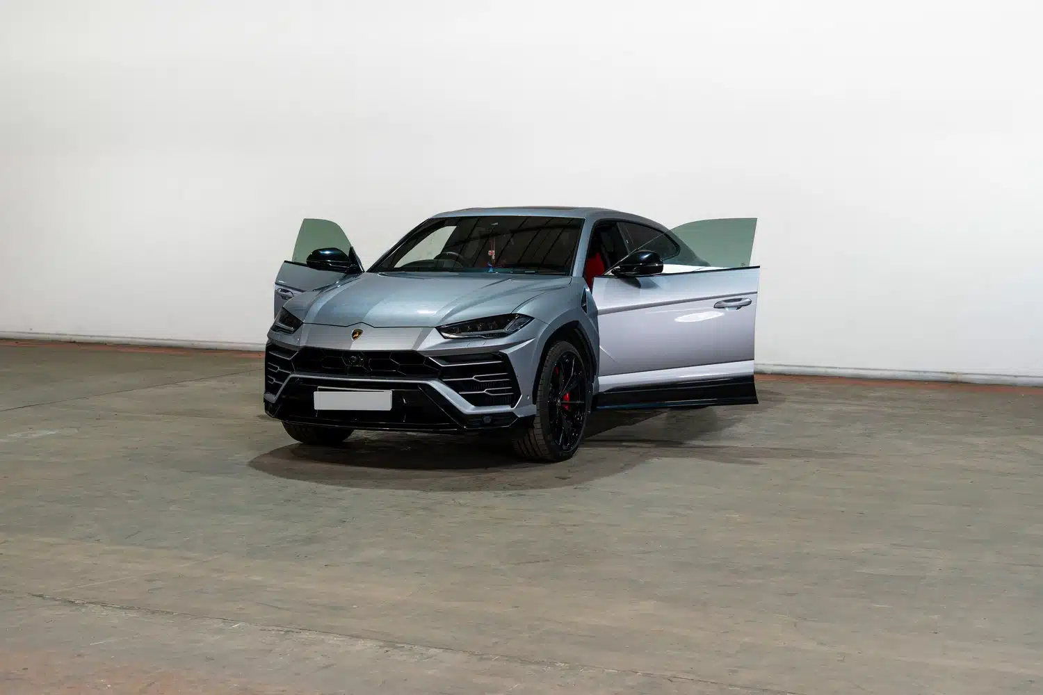A grey, 2021 Lamborghini Urus V8 Auto, facing forwards, in front of a white wall, in a warehouse, with it's front doors open